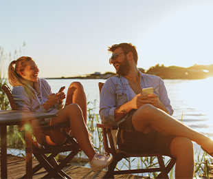 Man and woman sitting in chairs next to lake with sunset in the background