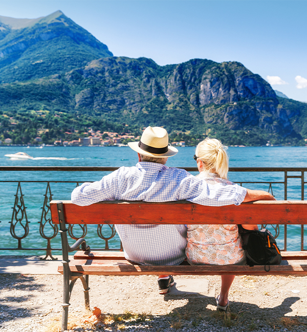 Man and woman sitting on a bench looking at water and mountain view