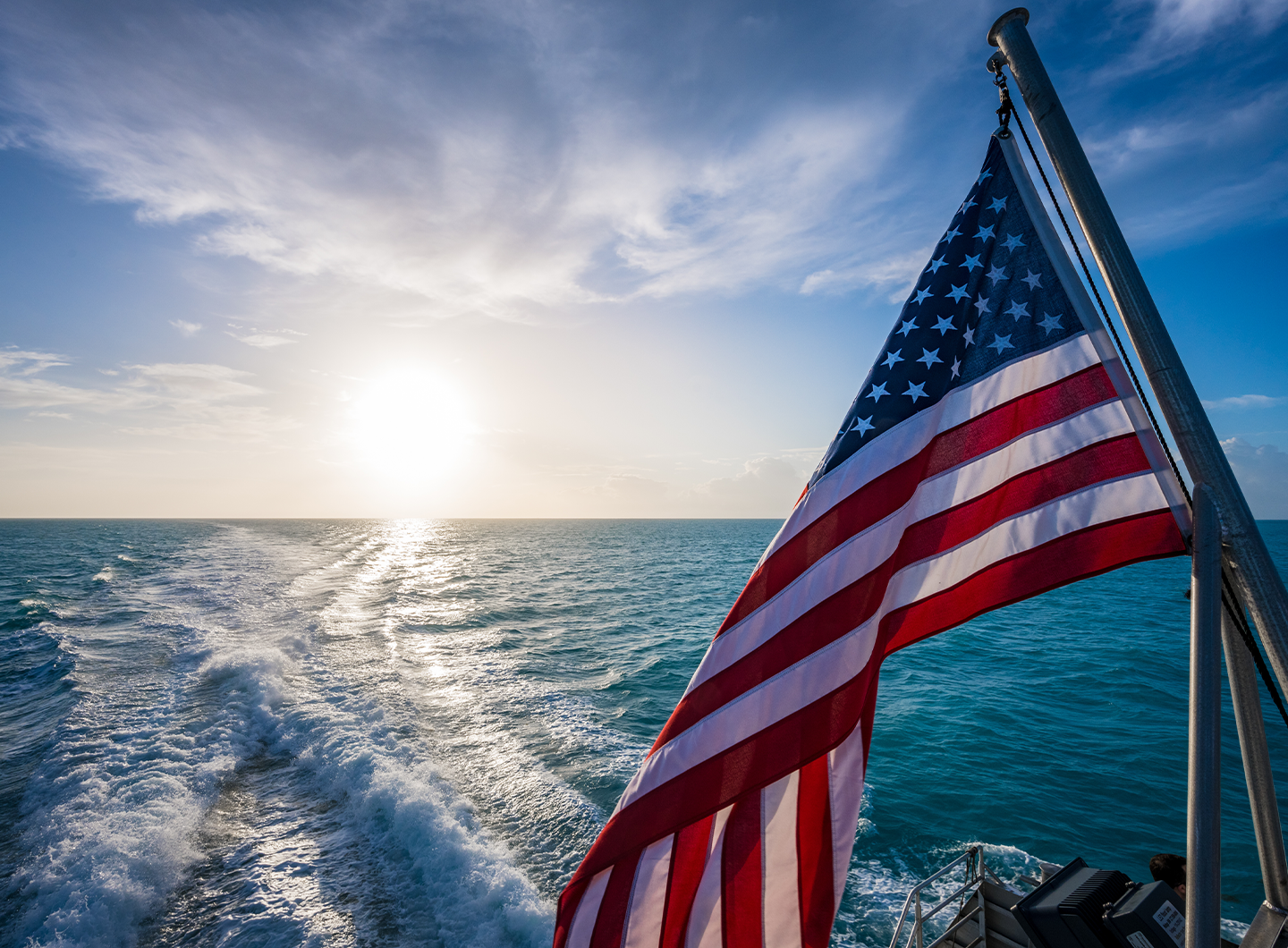 Flag waving over boat with ocean and sun