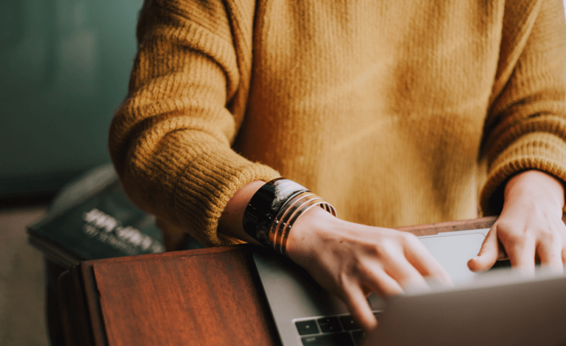 Person typing at computer with yellow sweater