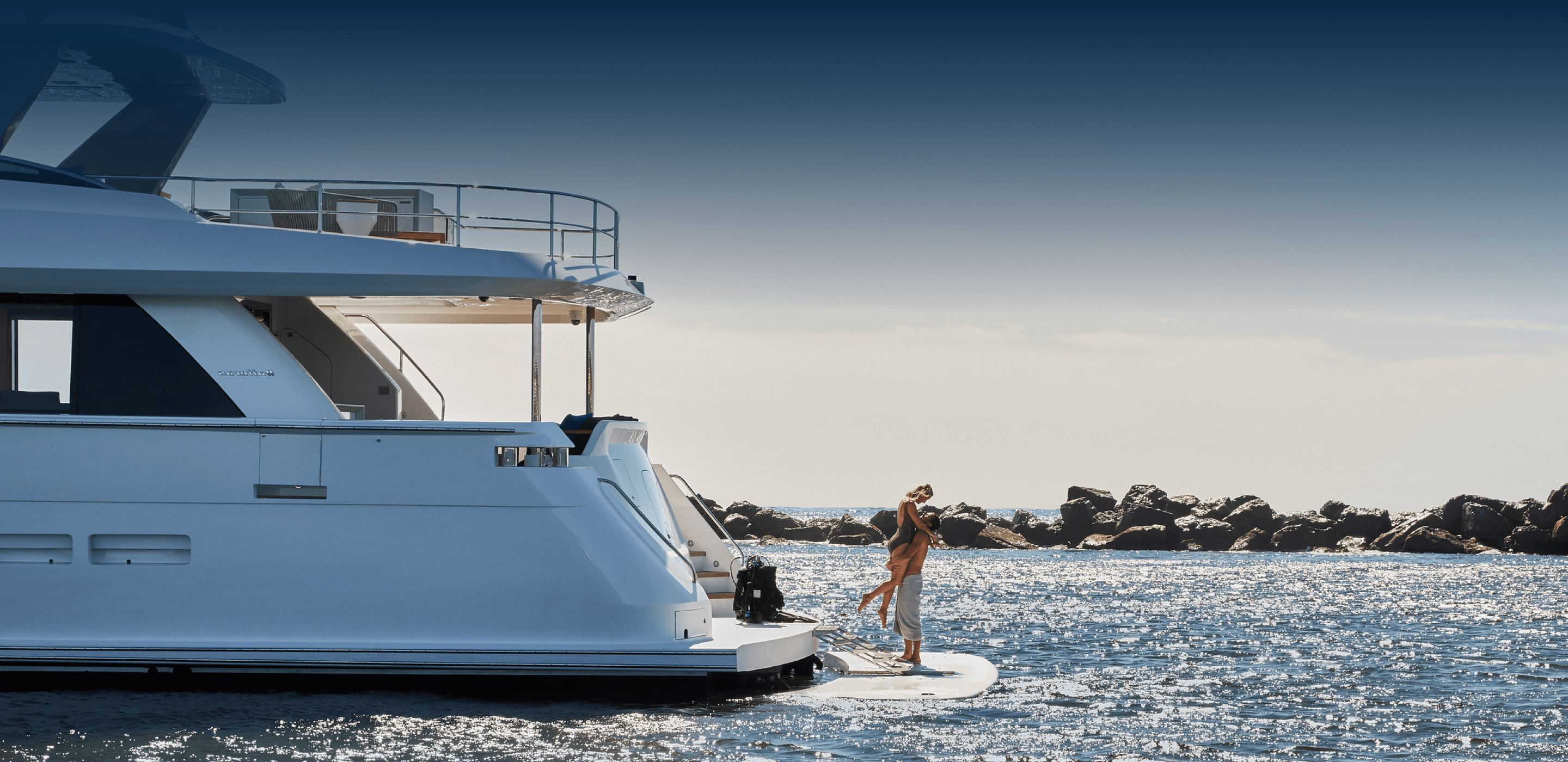 Couple hugging on back of yacht near rocks