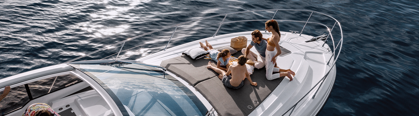 Family relaxing on a boat's deck, surrounded by calm water. They appear joyful, with a picnic basket nearby, creating a peaceful, sunny scene.