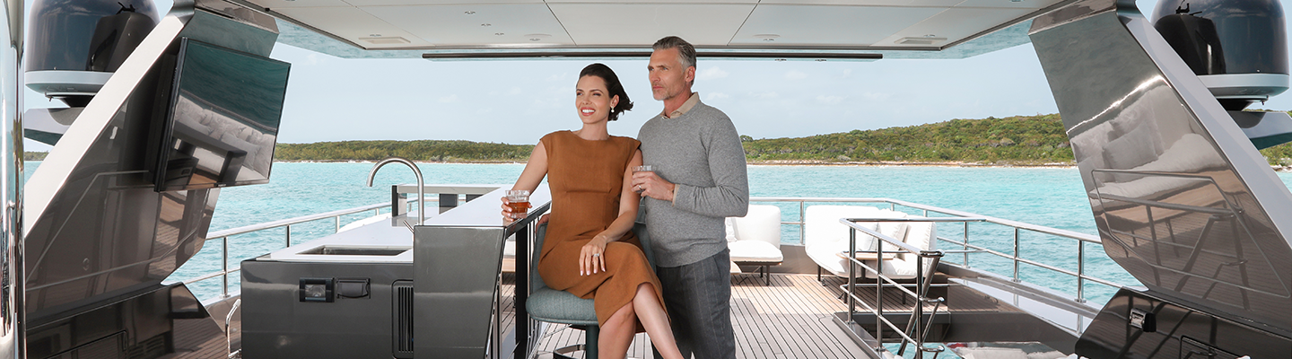 A man and woman relax on a yacht's deck, overlooking turquoise waters.