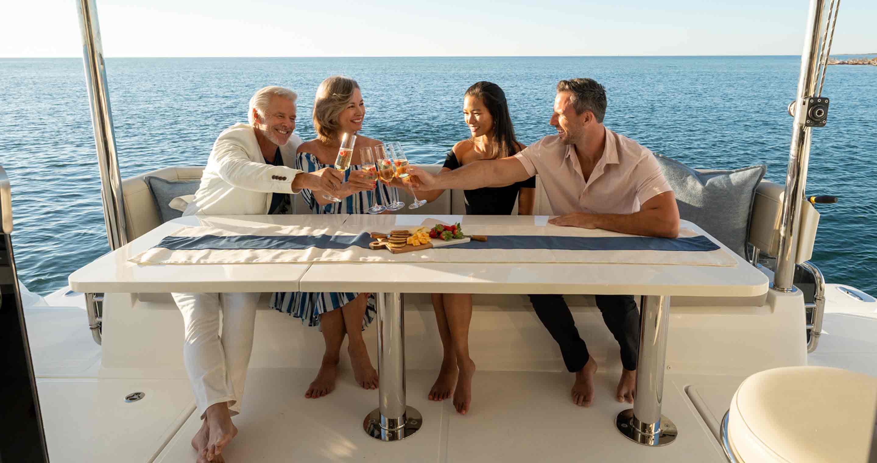 four people sitting at a table on a boat clanking glasses